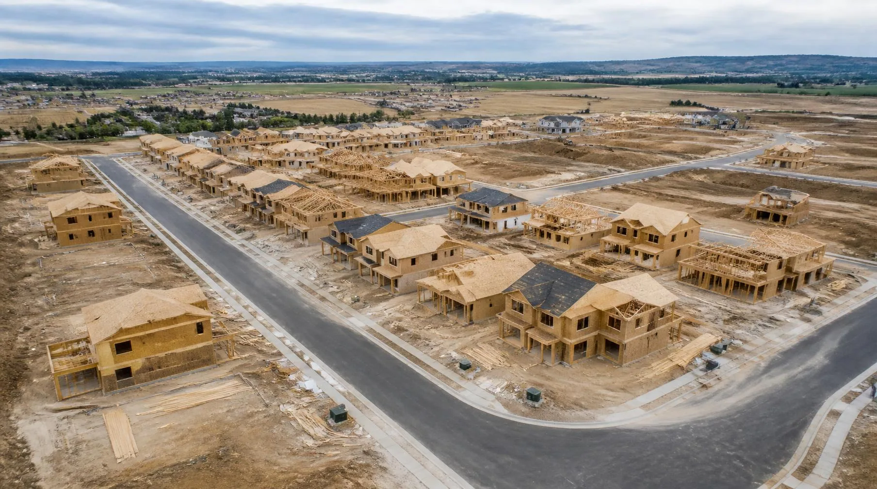 Aerial view of a residential subdivision under construction, with houses at framing and dry-in stage along new streets